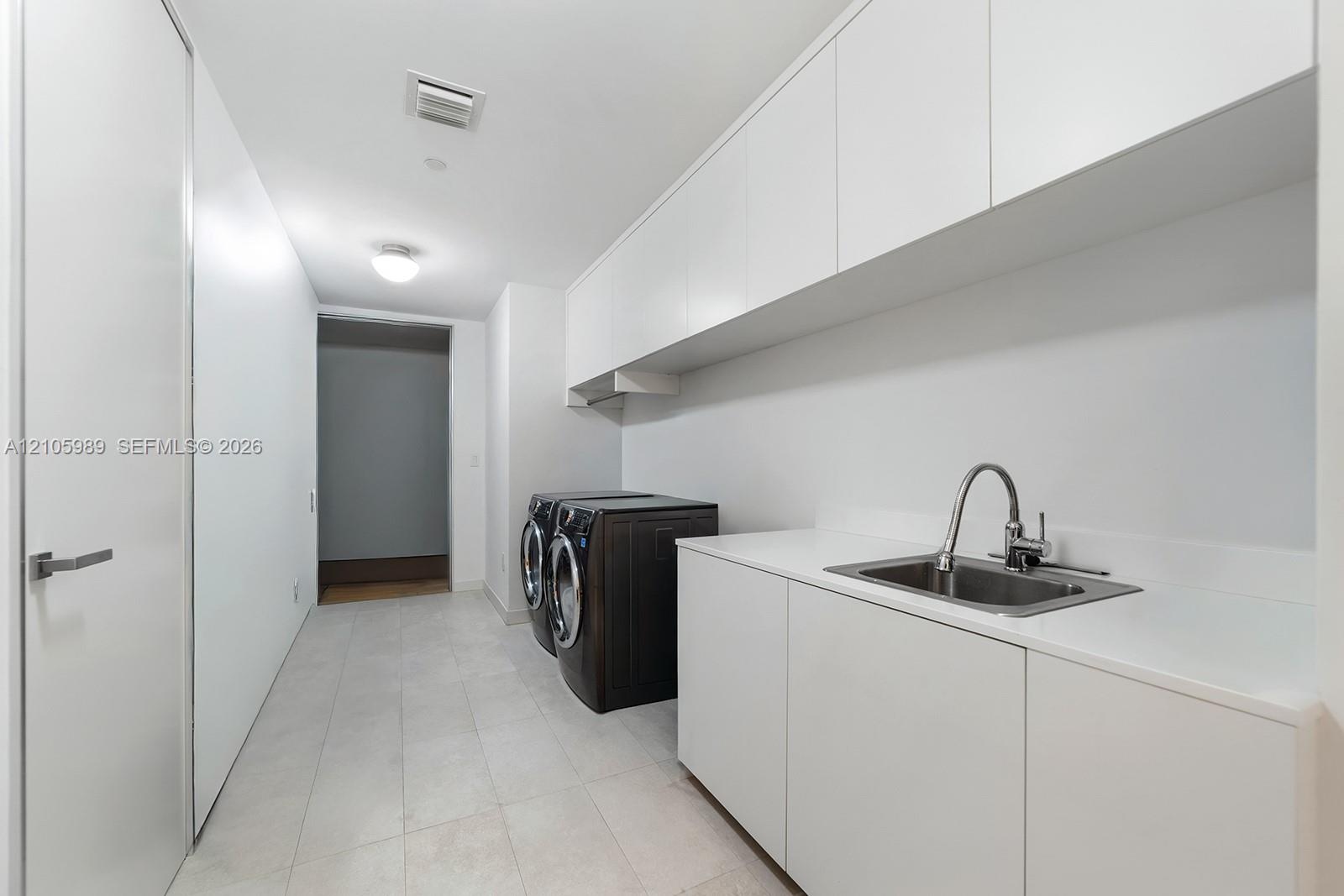 Utility space featuring expansive white cabinetry, white countertop, undermount stainless steel sink with a high-arch faucet, and large-format tile fl