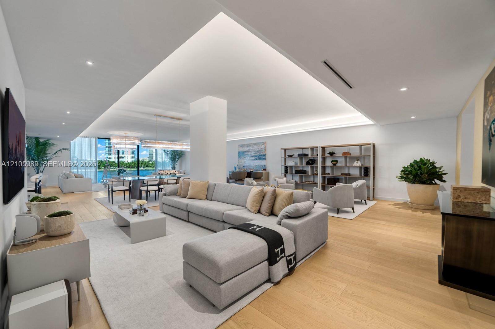 Open-concept living space featuring wood-finish flooring, recessed tray ceiling with integrated perimeter lighting, floor-to-ceiling windows, and rece