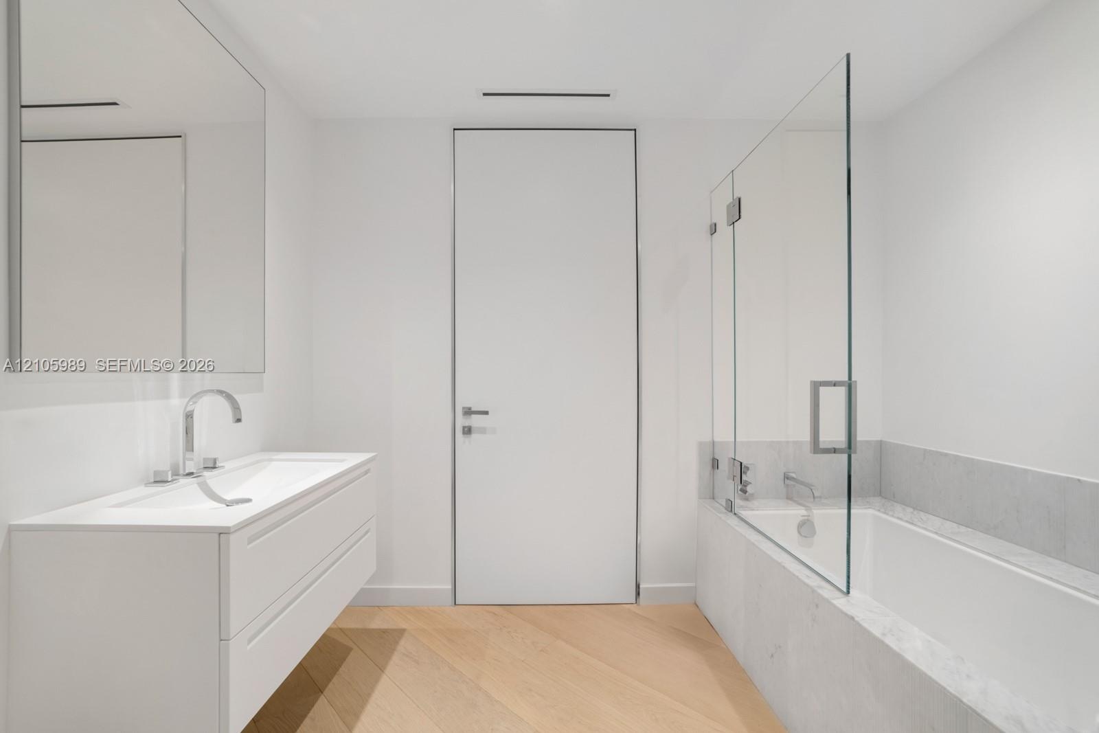 Wall-mounted floating vanity with integrated rectangular sink, wood-finish chevron flooring, frameless glass shower enclosure, and stone-surround soak
