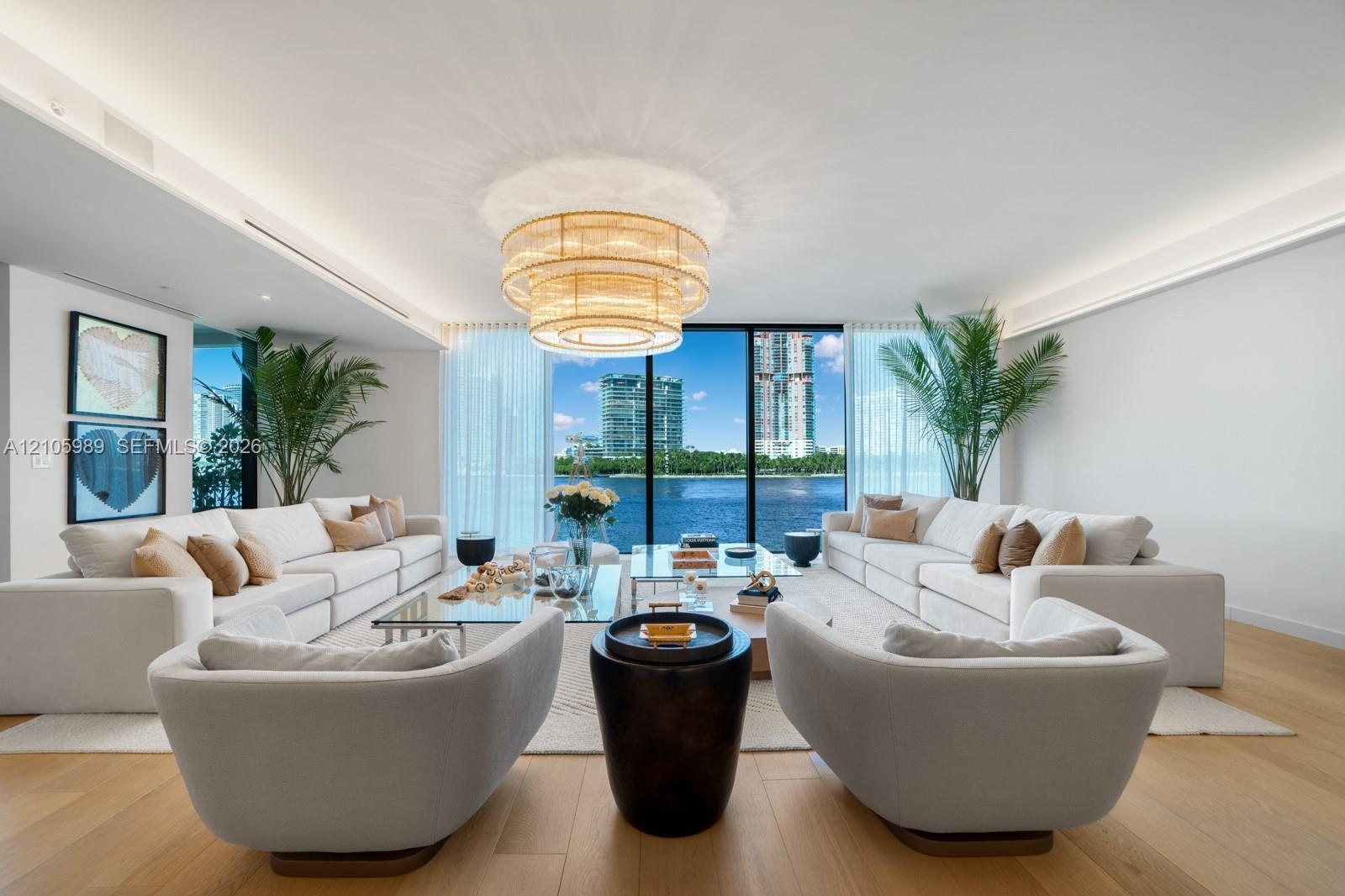 Open-concept living space featuring wood-finish flooring, recessed perimeter ceiling lighting, a tiered drum chandelier, and expansive floor-to-ceilin