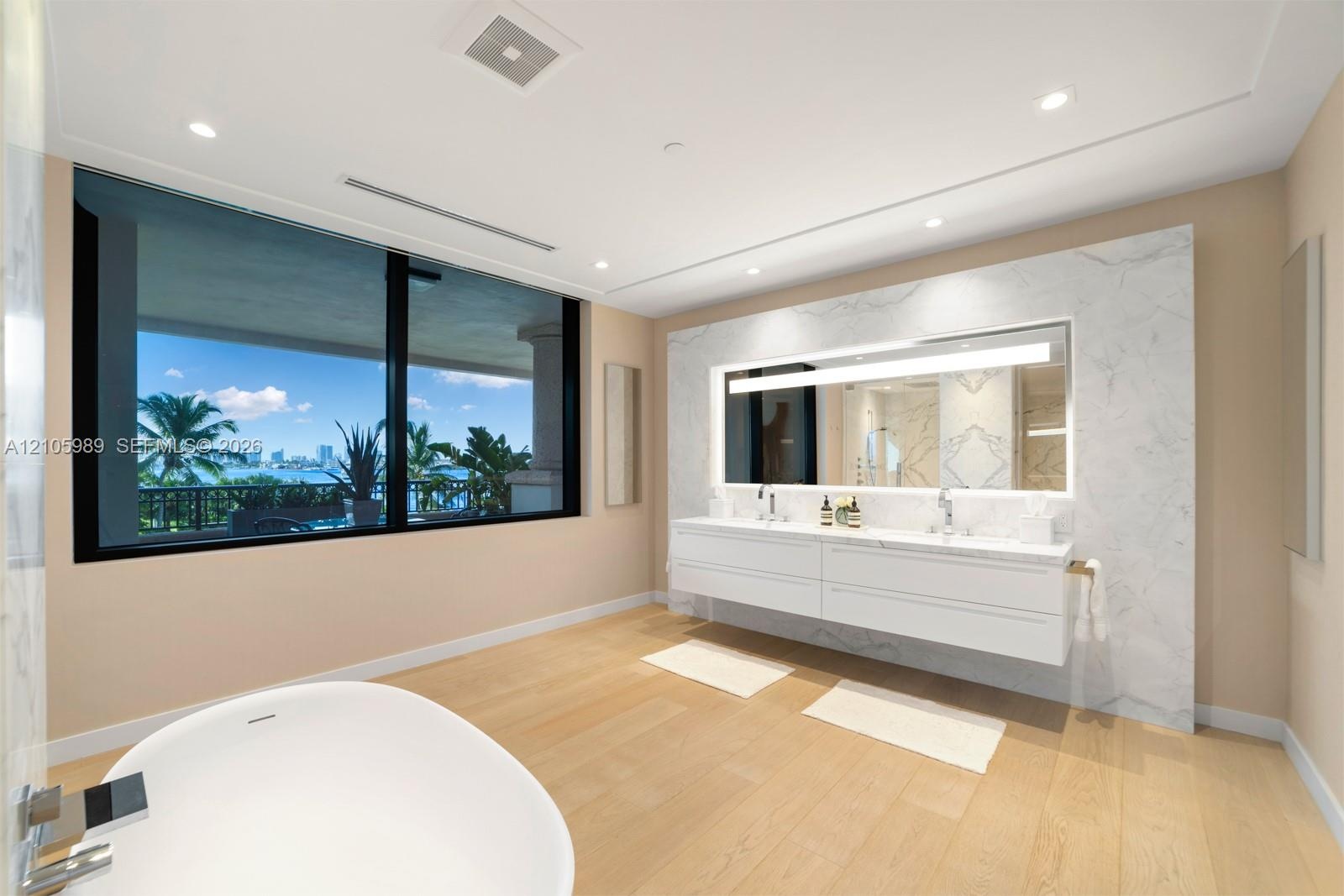 Floating dual vanity with integrated countertop, floor-to-ceiling stone wall treatment, back-lit mirror, freestanding soaking tub, and large-format bl