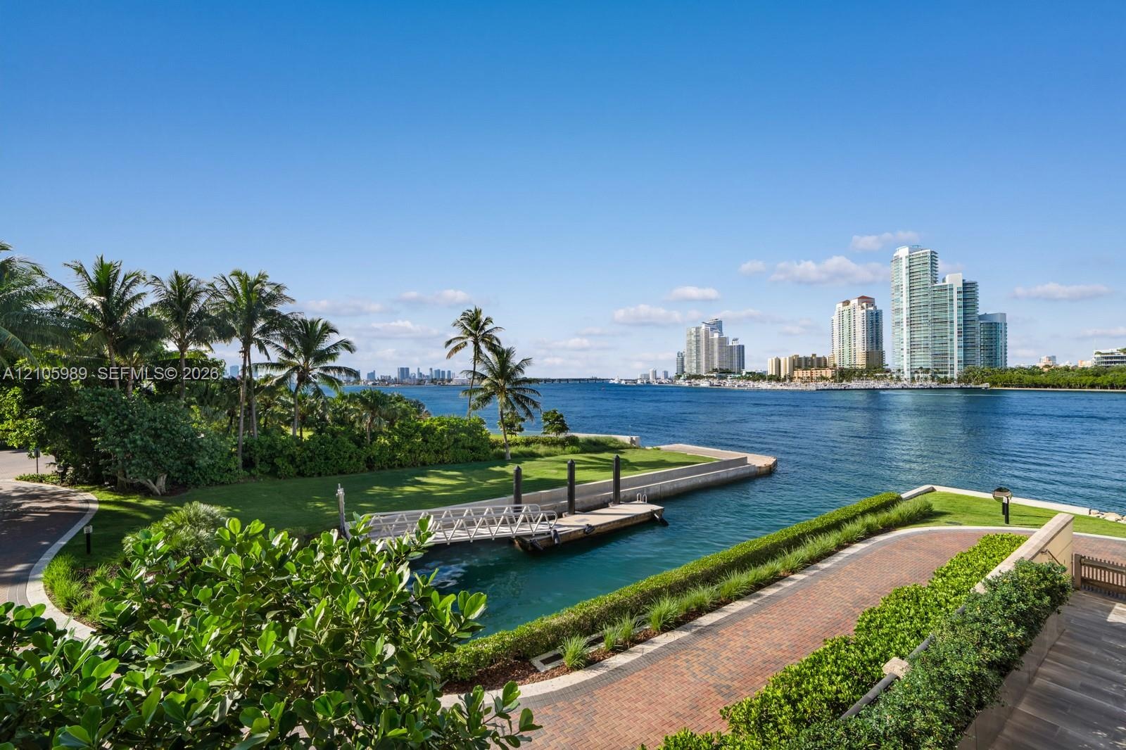 Waterfront property featuring a private boat dock, extensive paved driveway, manicured landscaping, and coastal scenery