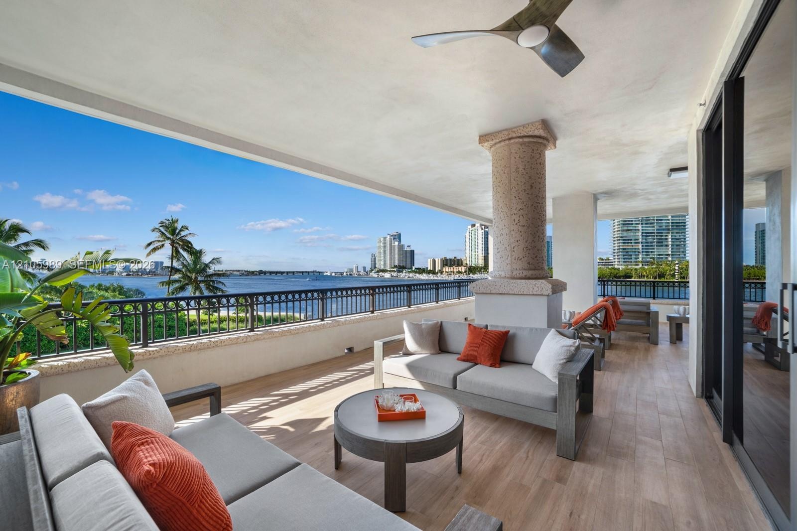 Covered balcony featuring wood-finish flooring, a textured stone column, black metal railing, and a mounted ceiling fan