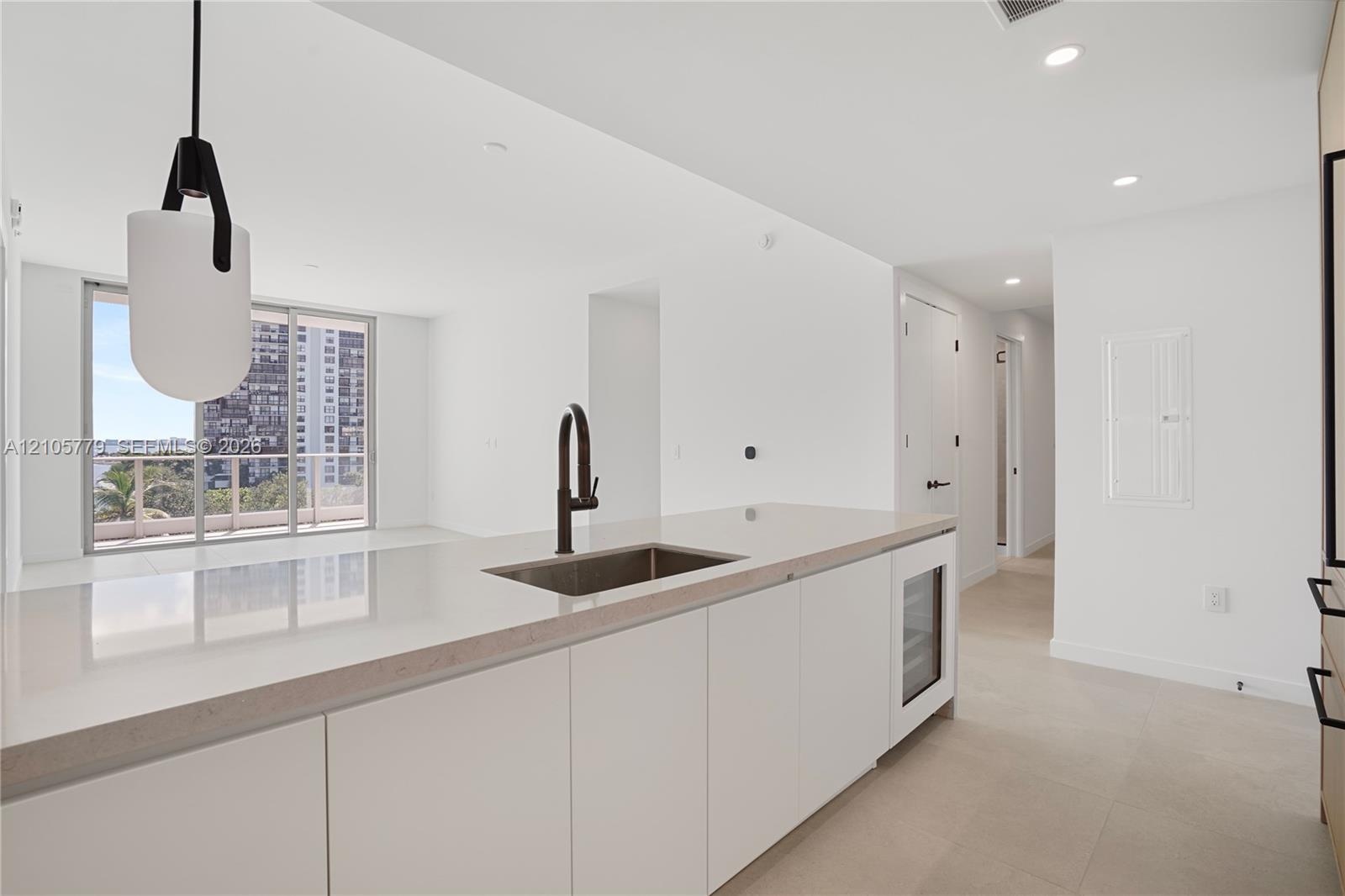 Kitchen island featuring a stone countertop, undermount sink with a matte black faucet, built-in under-counter beverage chiller, and modern pendant li