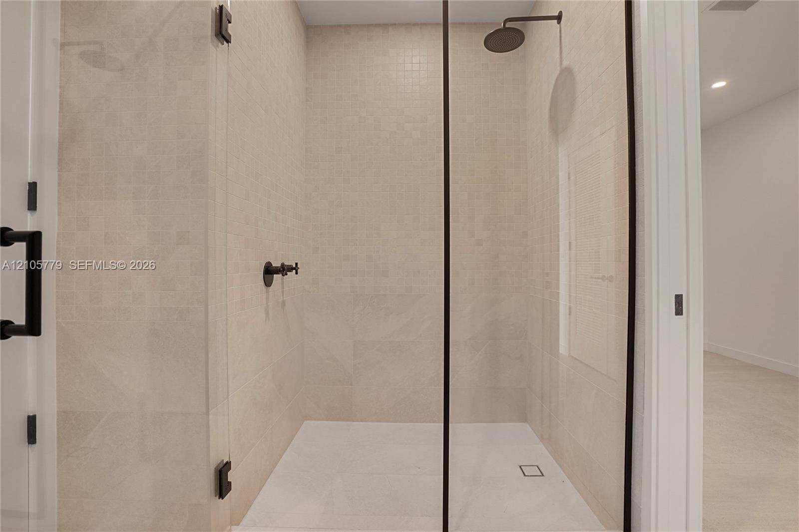 Walk-in shower featuring floor-to-ceiling neutral tile, glass enclosure with matte black hardware, rainfall showerhead, and wall-mounted matte black f