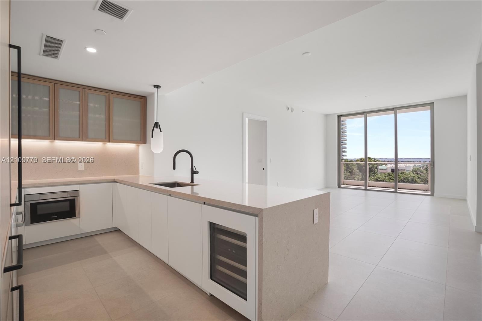 Modern kitchen featuring white flat-panel cabinetry, light-toned stone countertops, a waterfall-edge island, built-in wine refrigeration, and a matte 