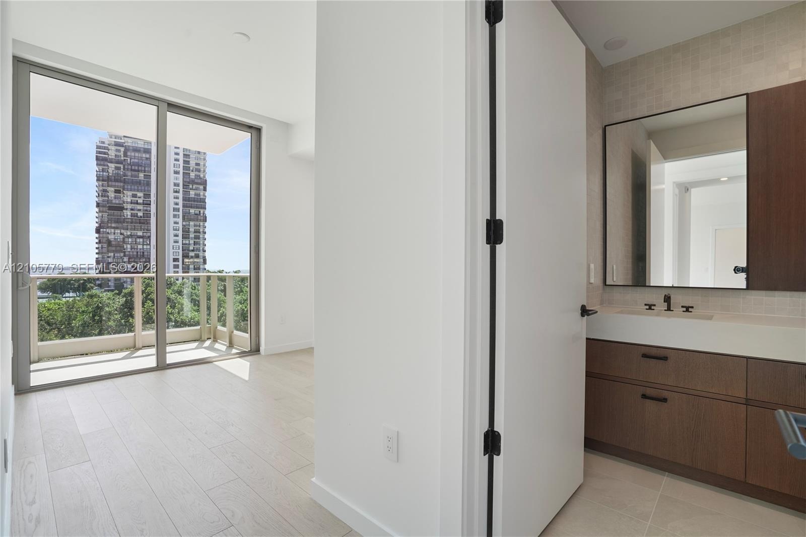 Floor-to-ceiling sliding glass door, private balcony, wood-finish flooring, floating vanity with dual-toned cabinetry, and large rectangular wall mirr