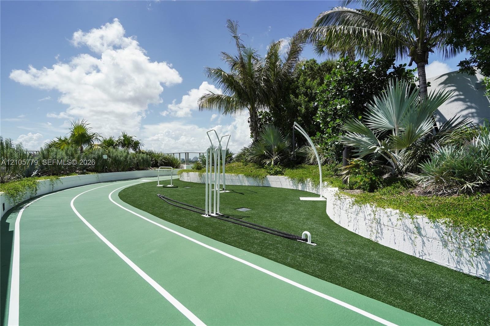 Outdoor fitness circuit featuring a synthetic running track, artificial turf area, built-in exercise equipment, and tiered stone retaining walls surro