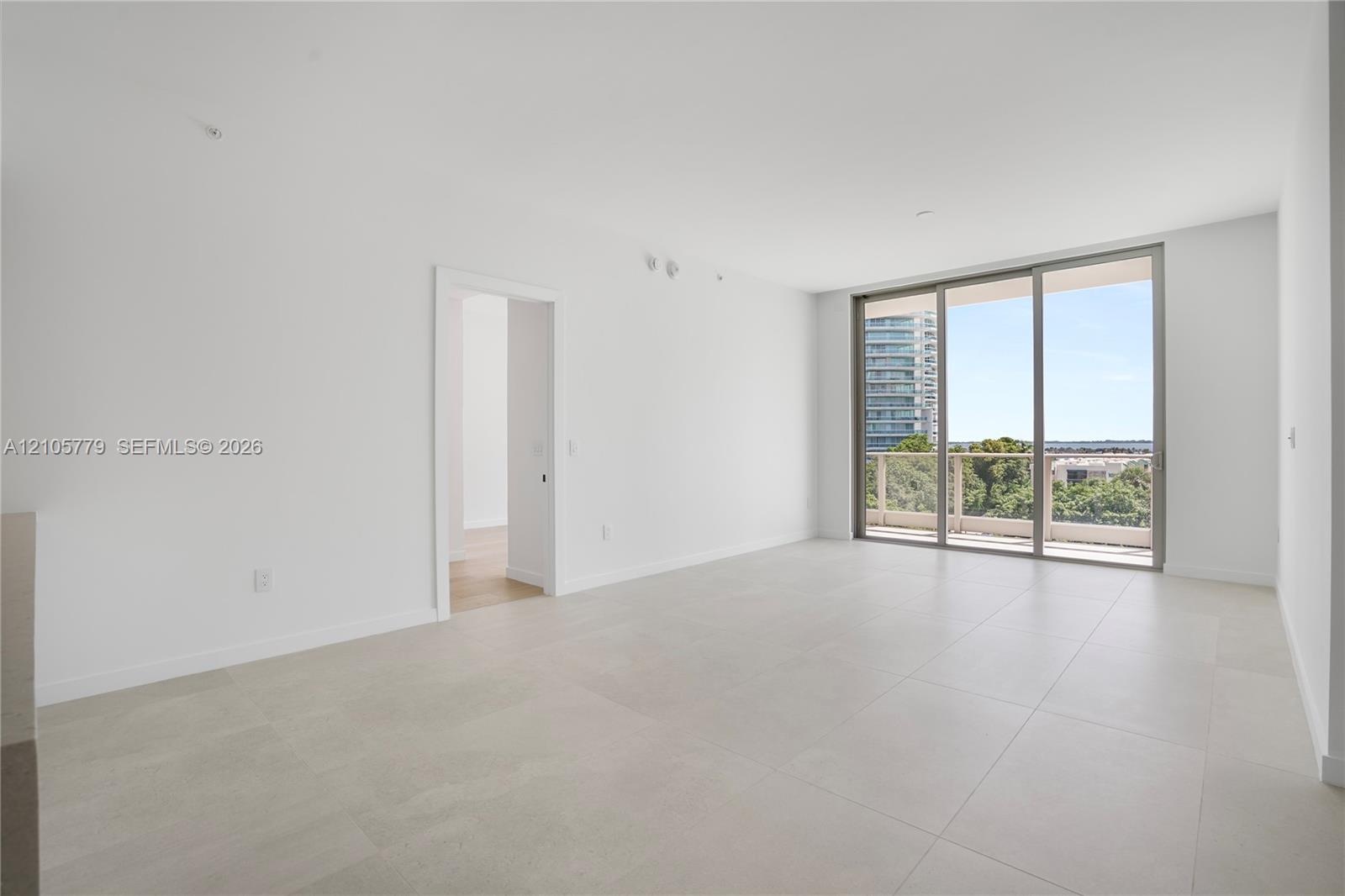 Open-concept interior featuring large-format tile flooring, recessed lighting, and floor-to-ceiling sliding glass doors opening to a balcony