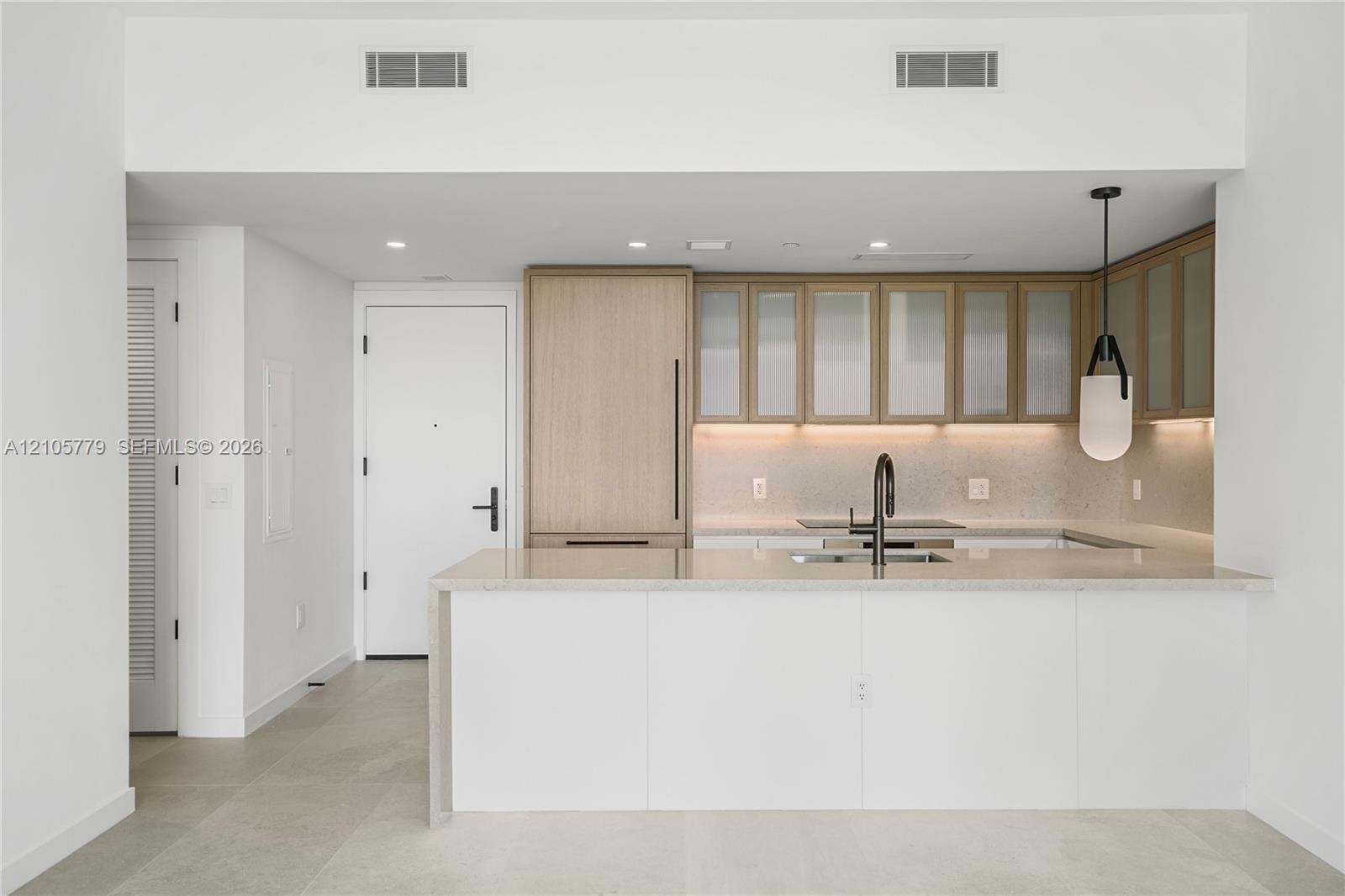 Kitchen featuring light wood-finish cabinetry with frosted glass inserts, a white quartz waterfall-edge island, integrated refrigerator, matte black g