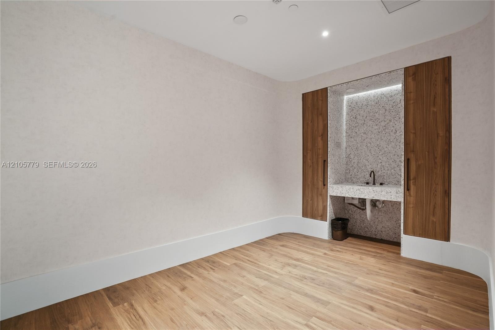 Room featuring wood-finish flooring, curved wall architecture, built-in floor-to-ceiling wood cabinetry, and a stone-surround recessed vanity with int