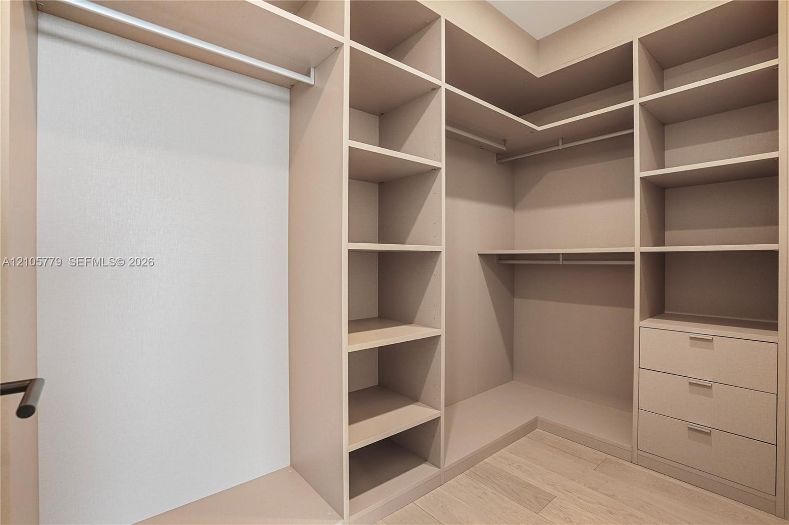 Walk-in closet featuring custom built-in shelving, integrated hanging rods, three soft-close storage drawers, and light-tone wood-finish flooring