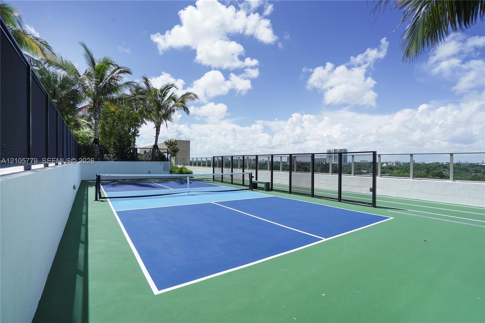 Rooftop recreation court featuring a multi-toned surface, black metal perimeter fencing, and glass paneling