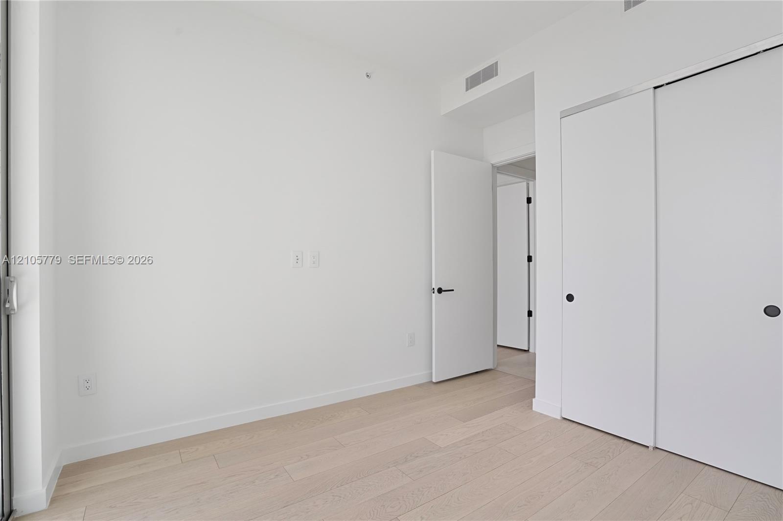 Room interior featuring light-toned wood-finish flooring, white walls, and a sliding-door closet with circular hardware