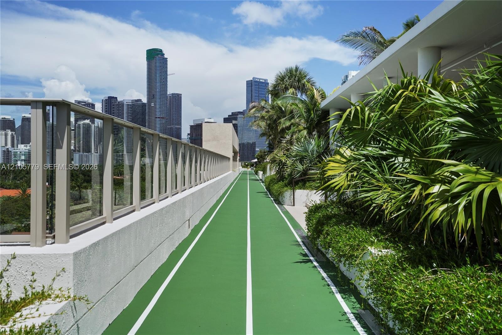 Outdoor running track featuring a high-traction surface, glass panel perimeter railing, and built-in landscape planters containing mature palm trees a