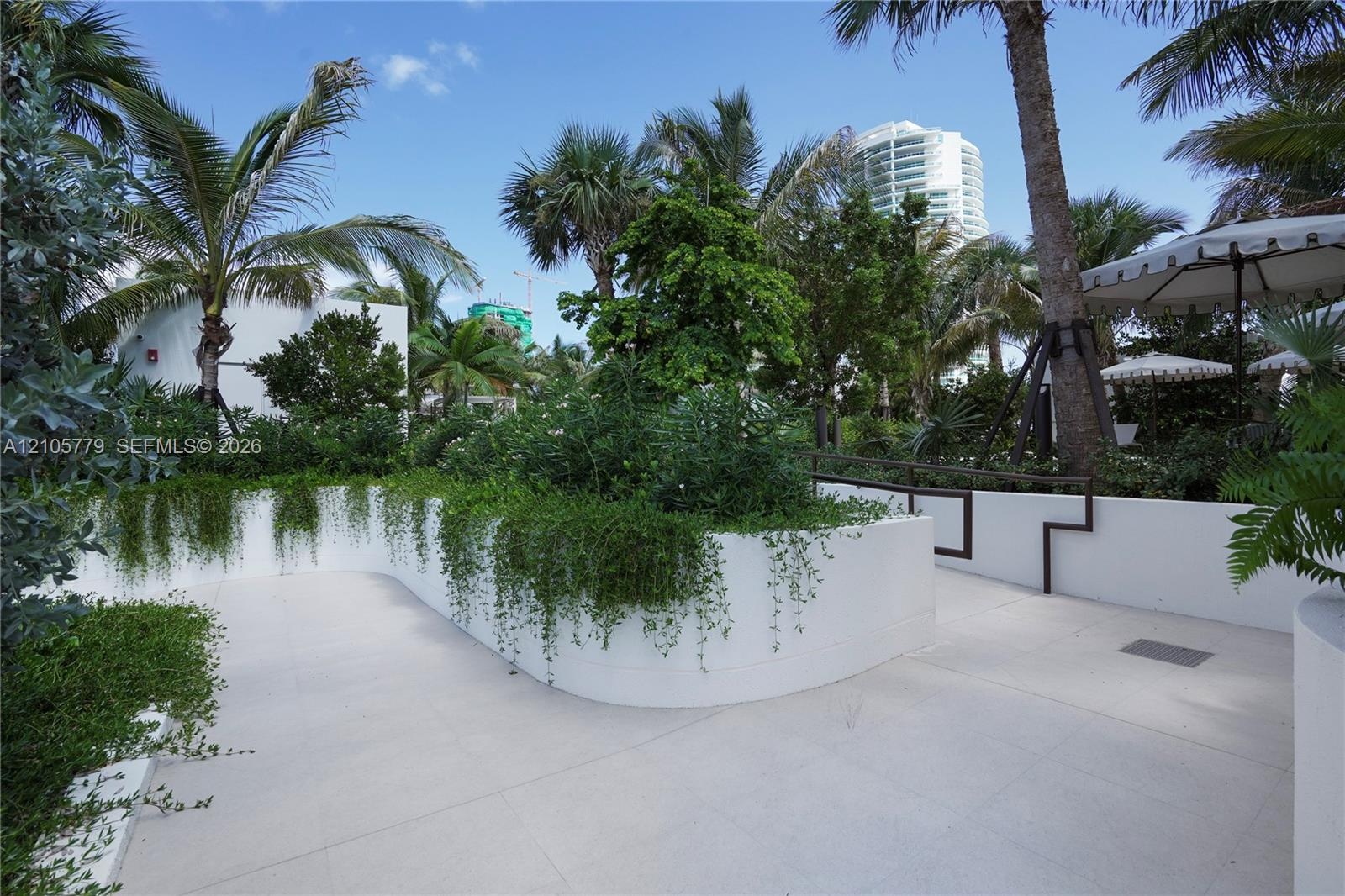 Landscaped grounds featuring curved white masonry planters, stone-finish paving, mature palm trees, and dense greenery