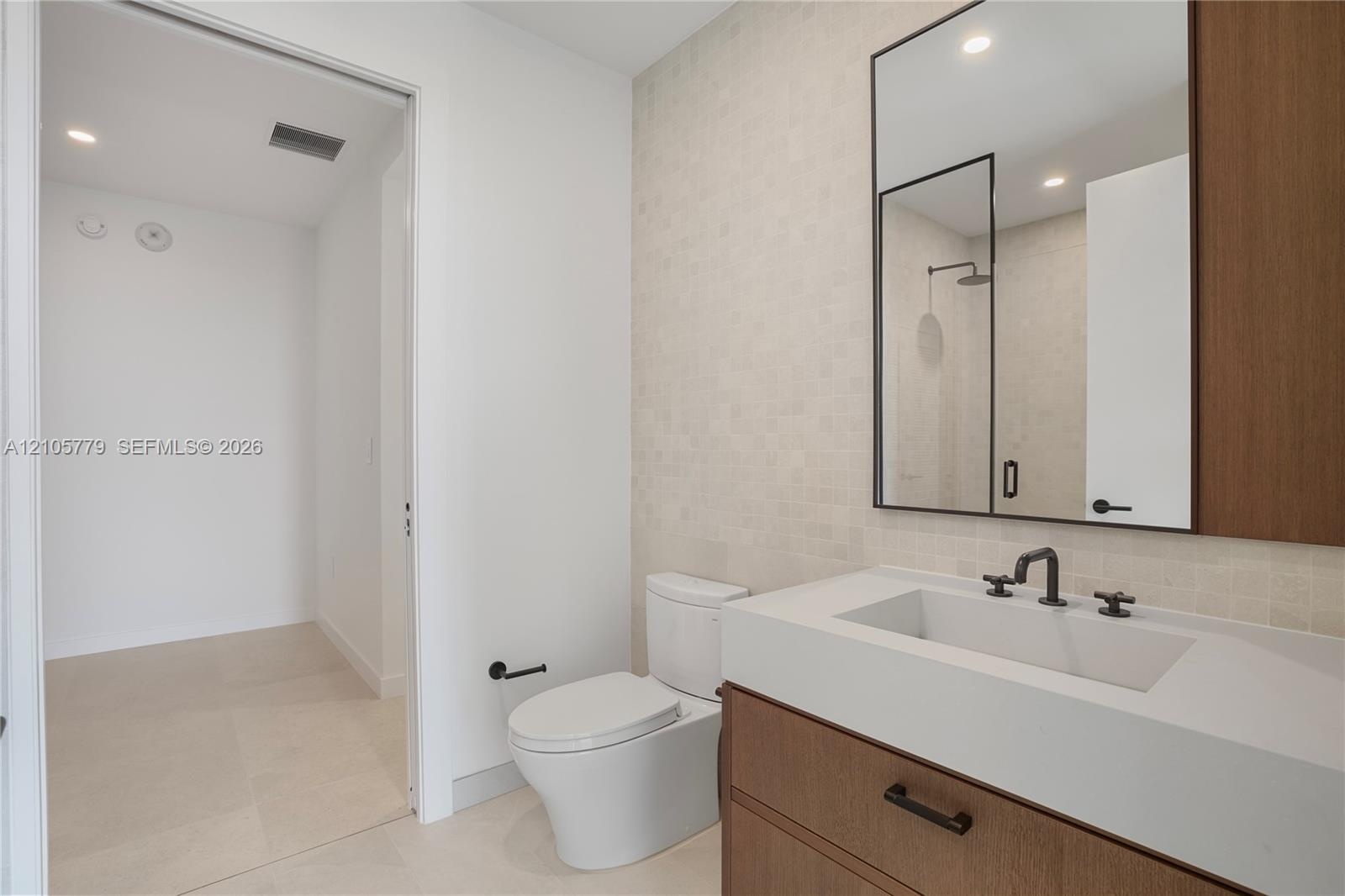 Floating wood-finish vanity with a stone countertop, rectangular undermount sink, matte black widespread faucet, and matching framed mirror, complemen