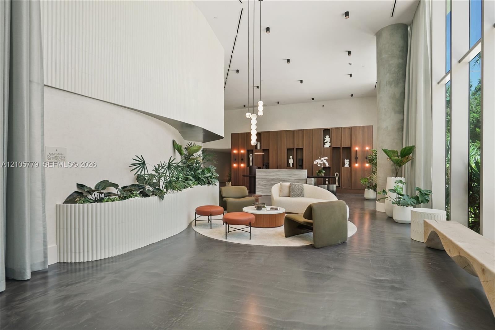 Lobby featuring high ceilings, floor-to-ceiling windows, curved architectural wall with integrated planter, dark smooth-finish flooring, and wood-pane