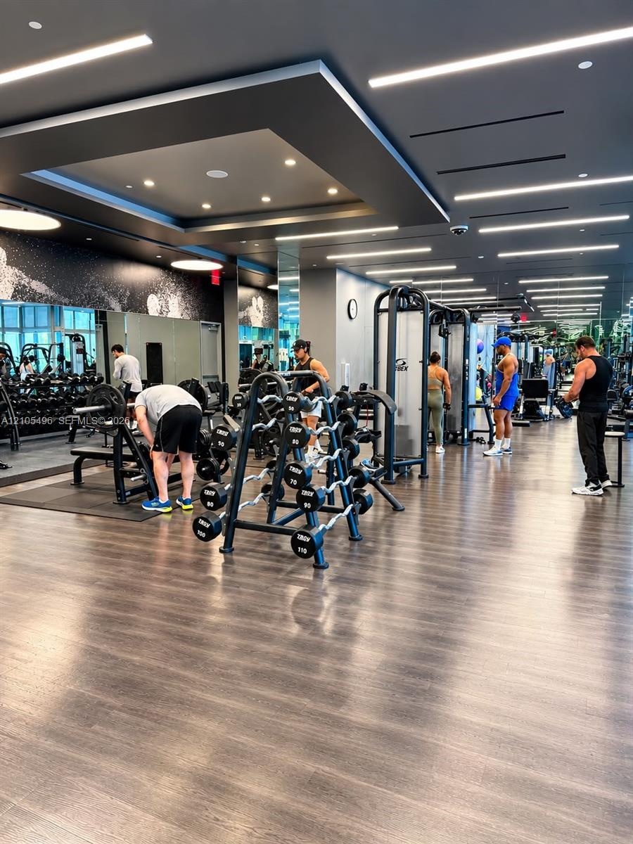 Fitness center featuring wood-finish flooring, a recessed tray ceiling with integrated linear lighting, and wall-to-wall mirrors