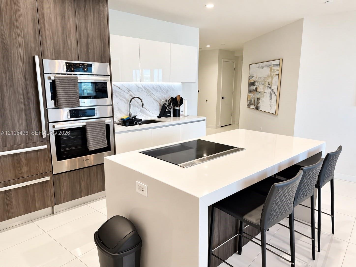 Kitchen featuring high-gloss white cabinetry, wood-finish floor-to-ceiling pantry units, a large quartz-topped island with an integrated induction coo