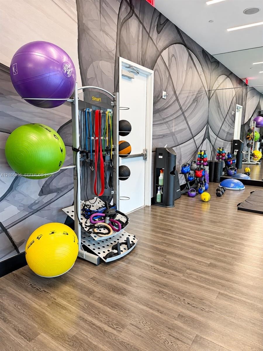 Fitness center featuring wood-finish flooring, floor-to-ceiling mirrored walls, and graphic wall mural