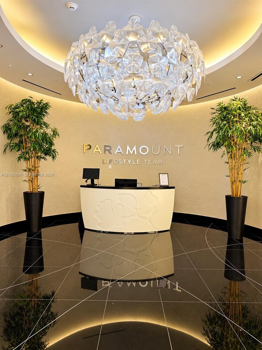 Rotunda entry featuring a large sculptural chandelier, polished black stone flooring with linear inlay patterns, textured wall finishes, and a custom 