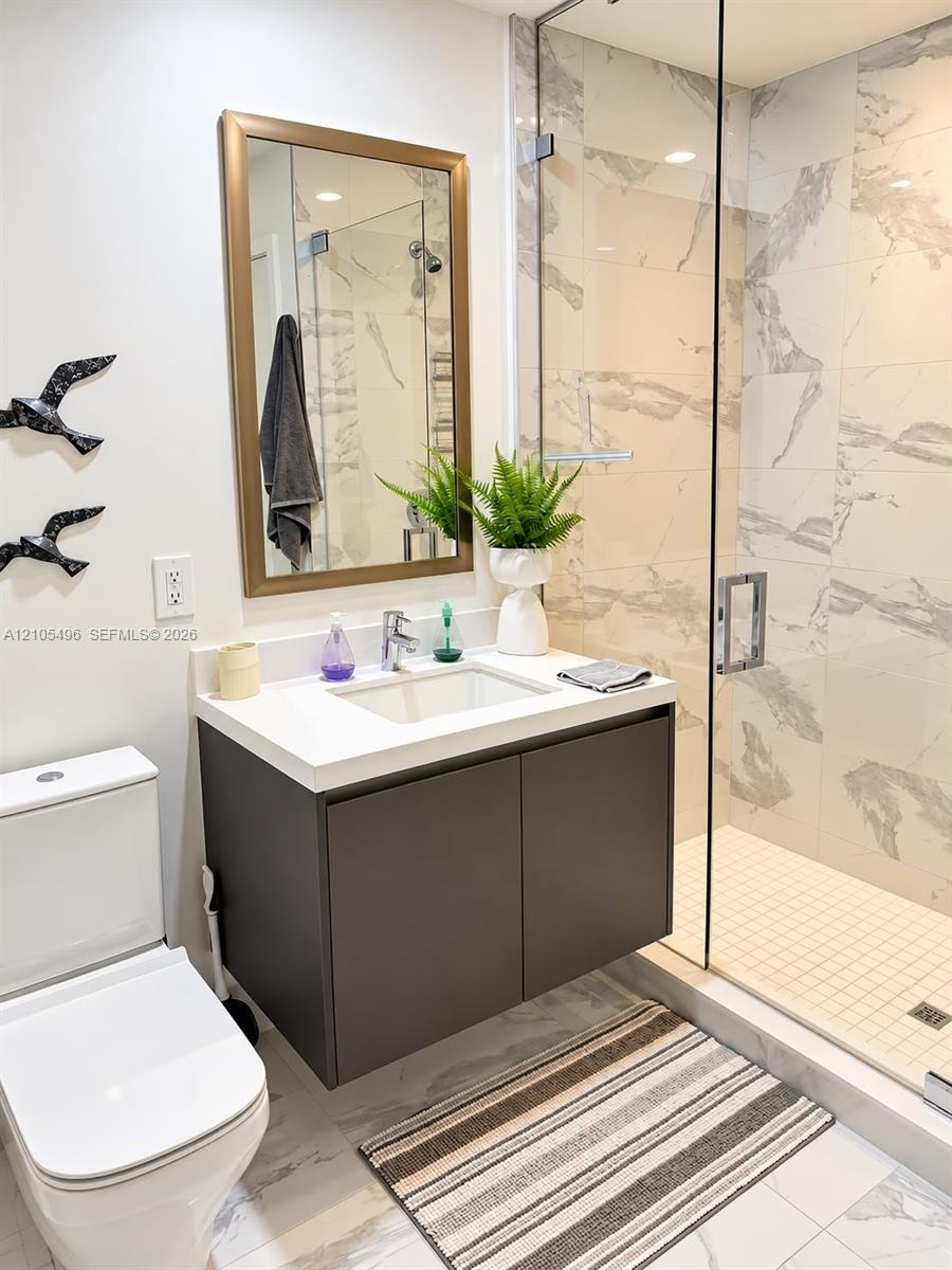 Wall-mounted vanity featuring a solid surface countertop, integrated sink, walk-in shower with floor-to-ceiling tile surround and glass enclosure, and