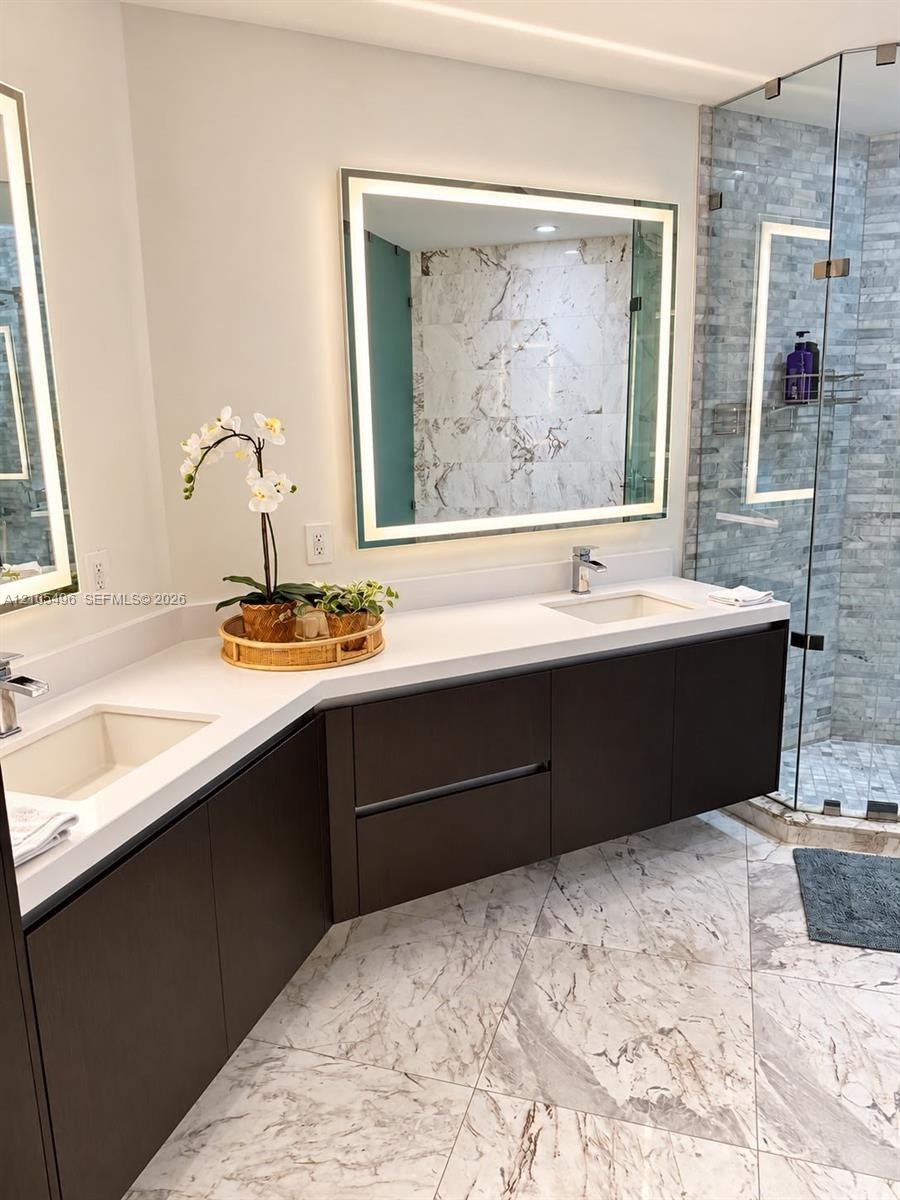 Floating dual vanity featuring dark cabinetry, solid-surface countertops, integrated rectangular sinks, and large, illuminated mirrors, complete with 