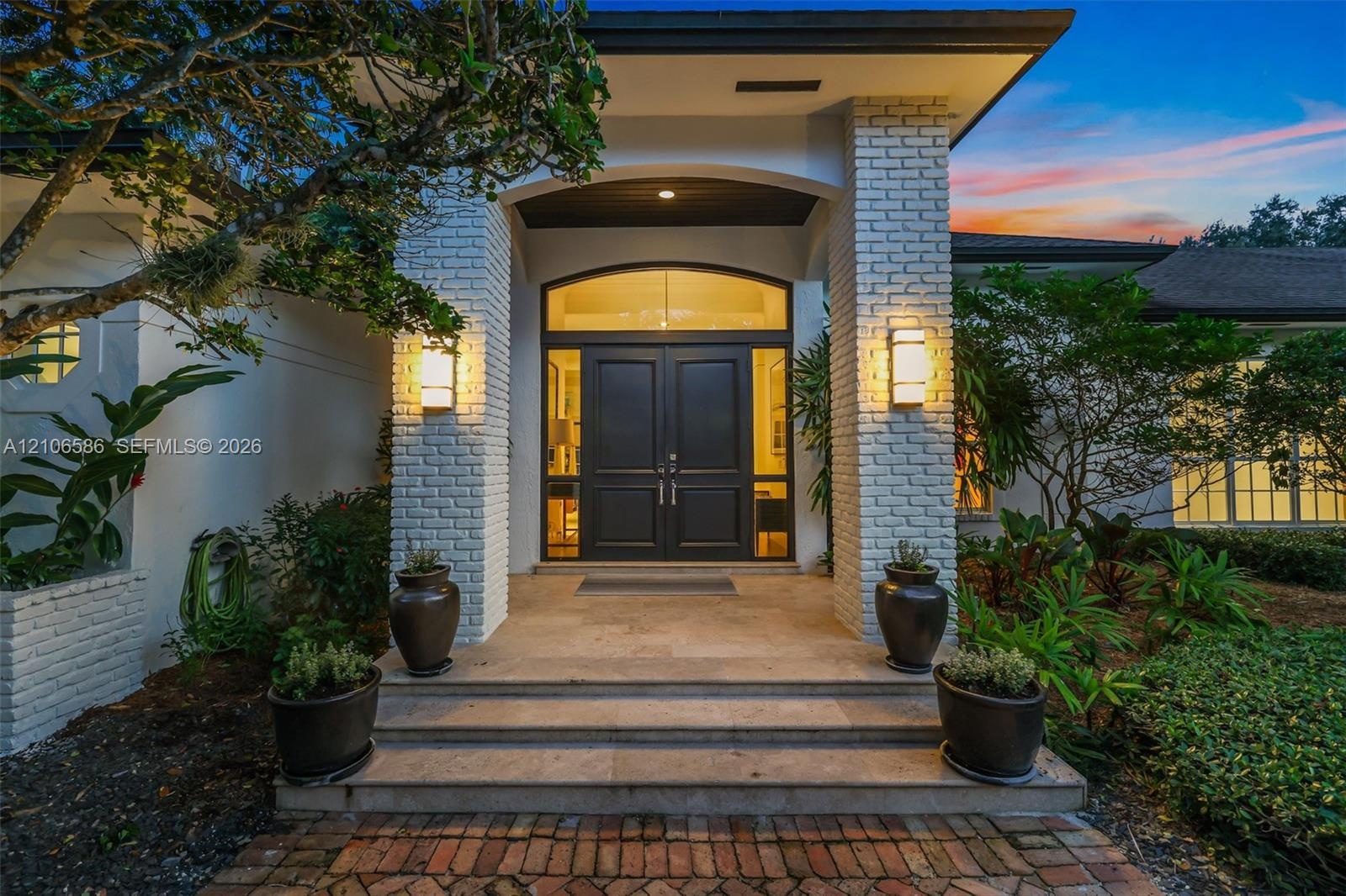 Exterior entrance featuring painted brick pillars, double front doors with an arched glass transom, stone step entry, and wall-mounted light fixtures