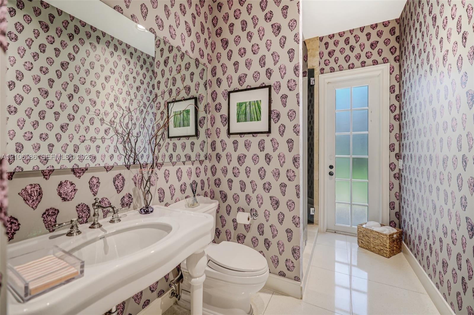 Pedestal sink with polished chrome widespread faucet, expansive wall-to-wall mirror, patterned wallpaper, and glass-paneled exterior door featuring ti