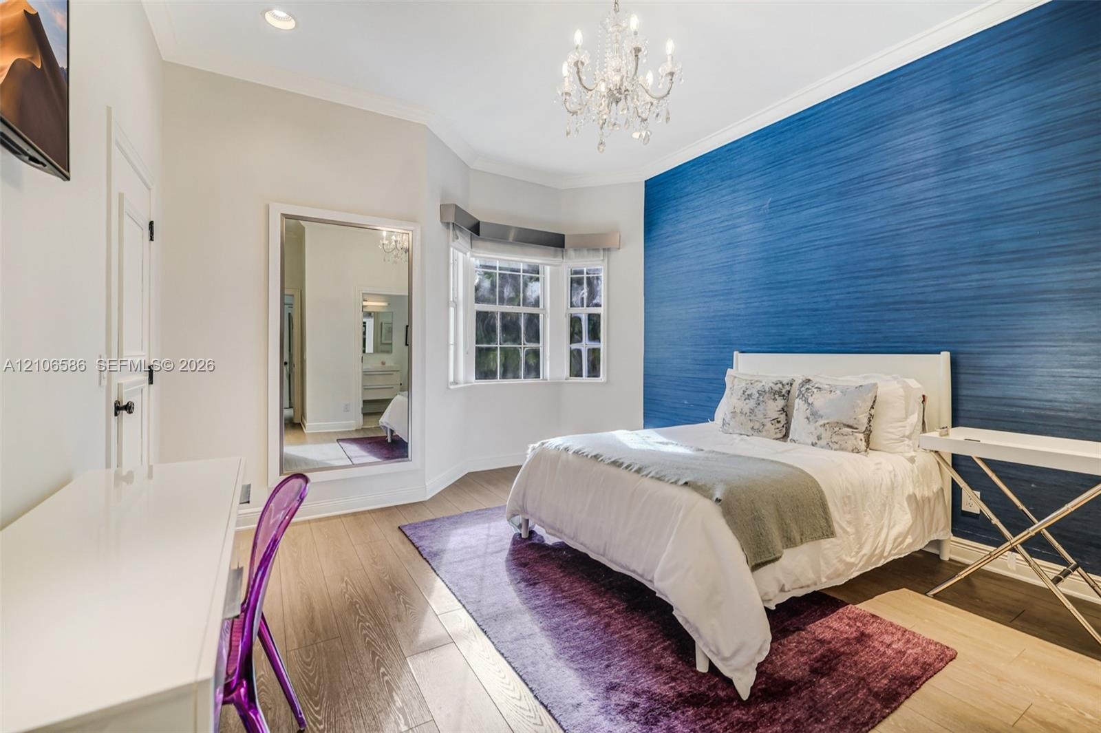 Bedroom featuring a deep blue textured accent wall, bay window, wood-finish flooring, recessed lighting, and a crystal chandelier