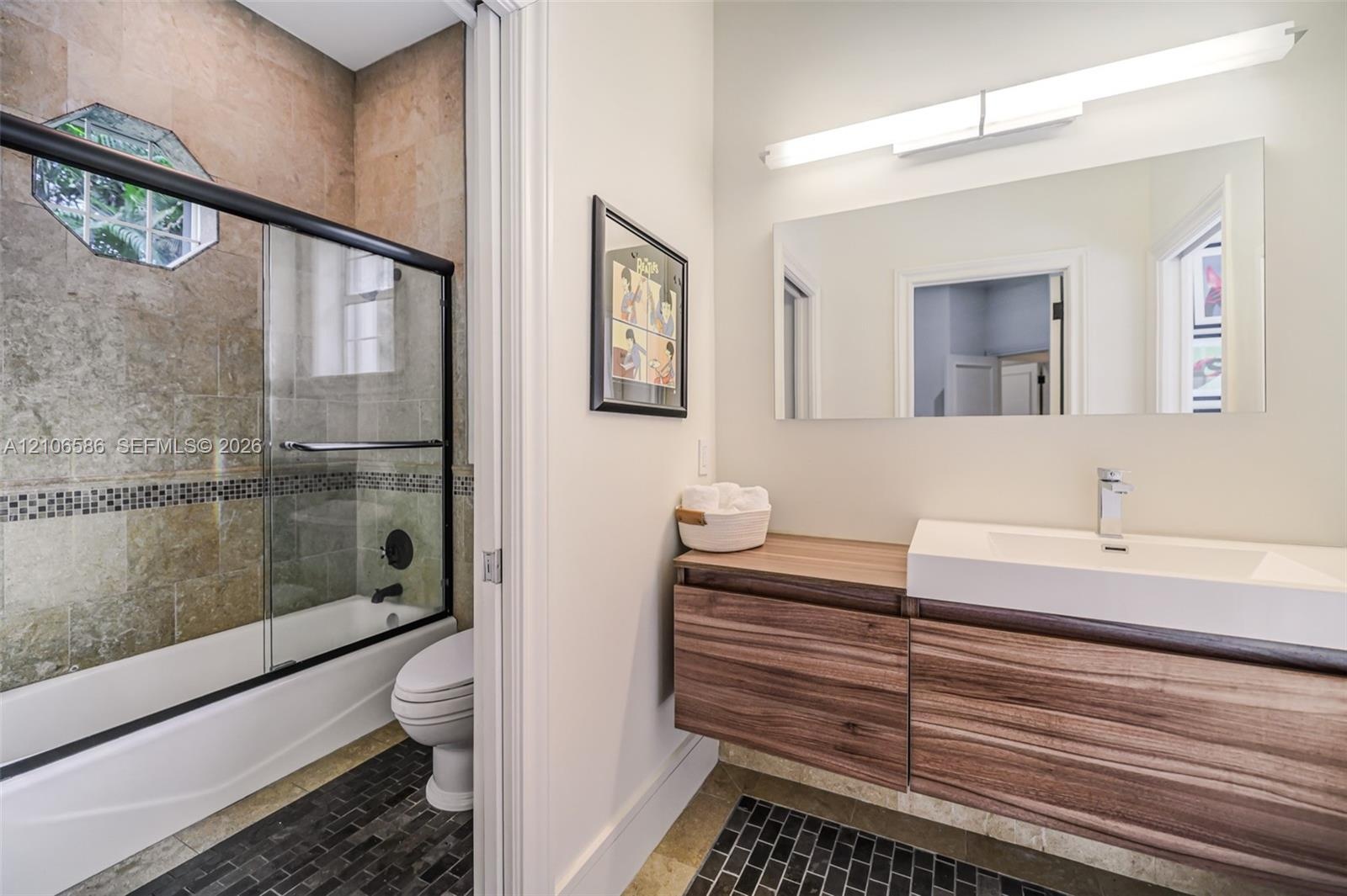Floating wood-finish vanity with a rectangular integrated sink, wall-mounted rectangular mirror, shower enclosure featuring a glass sliding door, and 