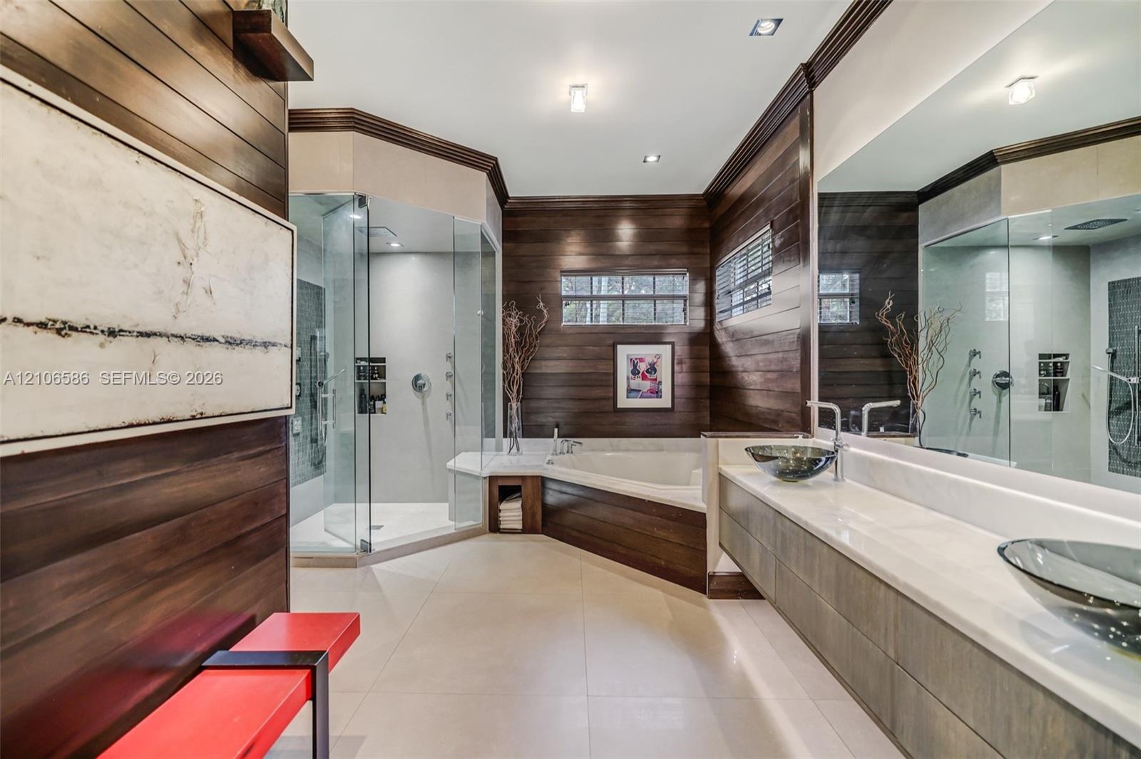 Custom bathroom featuring wood-paneled walls, a glass-enclosed shower, a jetted soaking tub, floating vanity with dual glass vessel sinks, and light-t