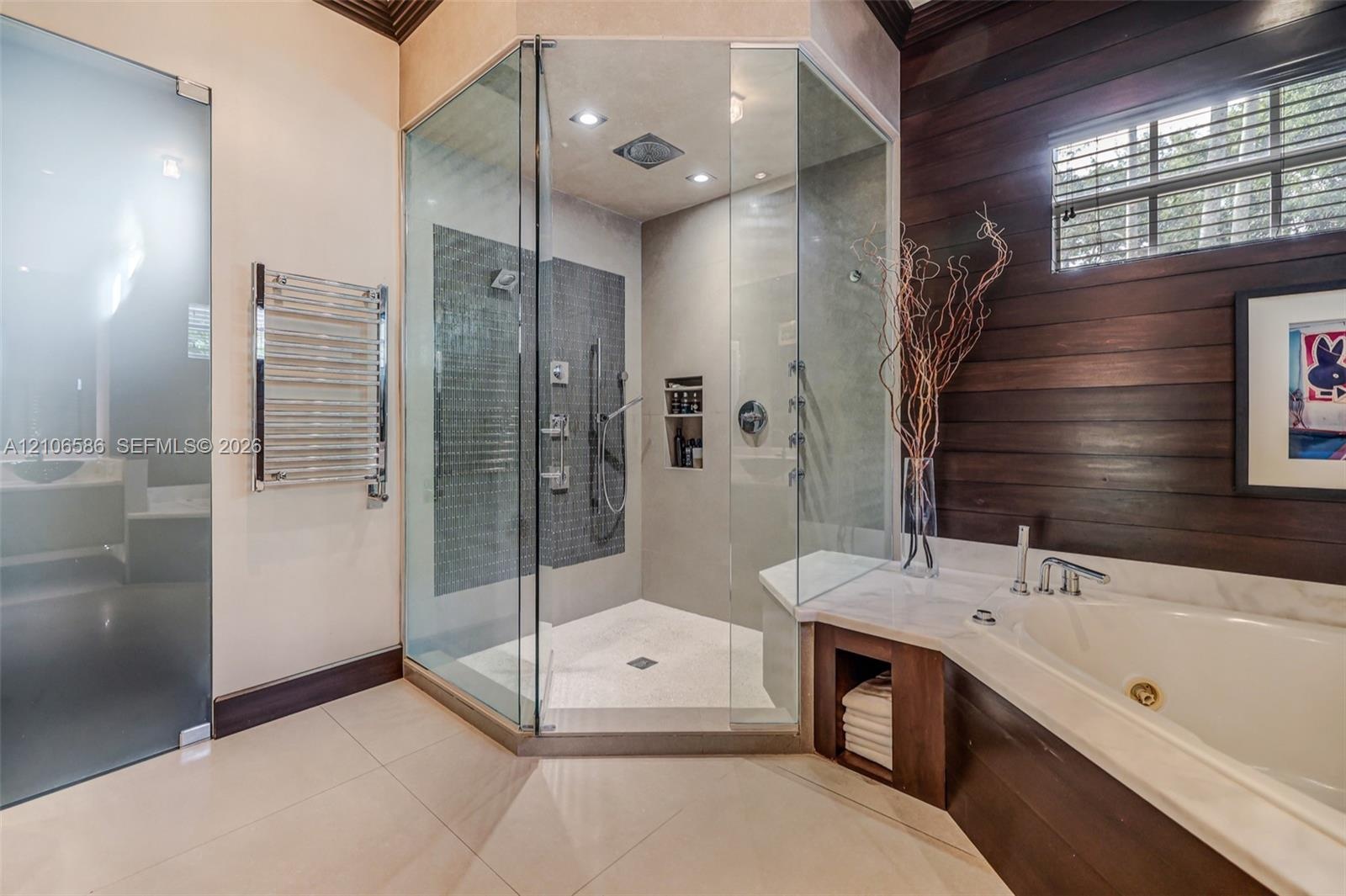 Walk-in glass shower with dual shower heads, deep soaking tub, wood-plank wall paneling, chrome heated towel rack, and large-format tile flooring