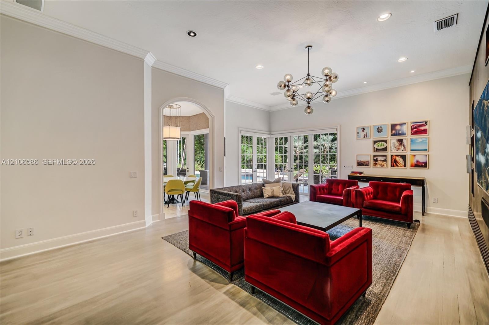 High-ceiling interior featuring wood-finish flooring, crown molding, multi-light geometric chandelier, and arched entryway
