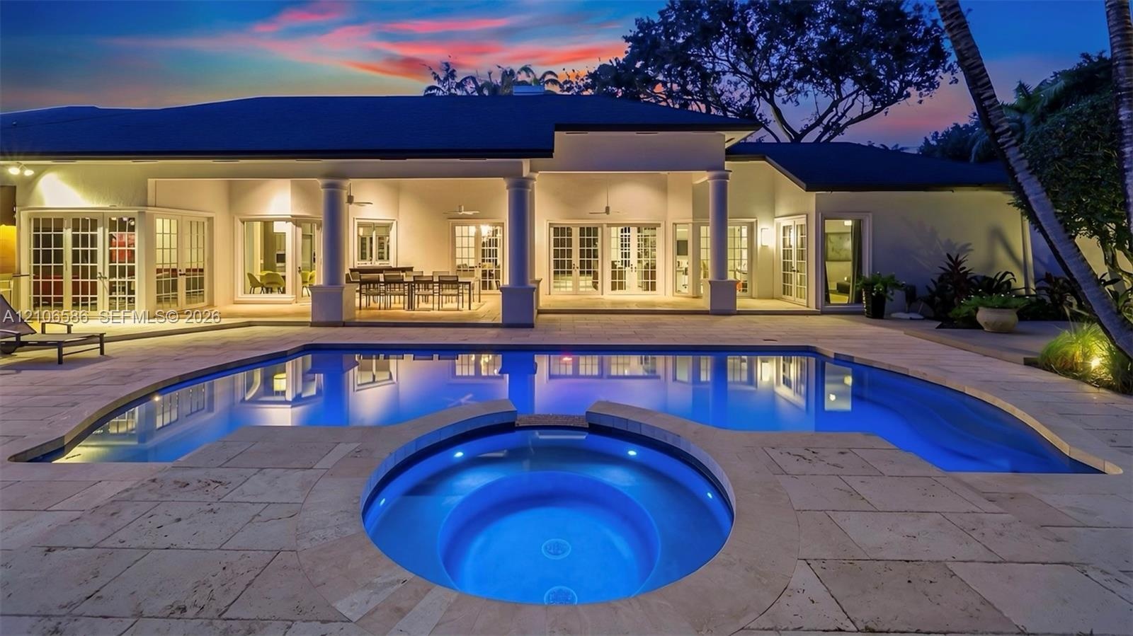Covered patio featuring structural columns, inground pool, integrated spa, and stone-paver decking