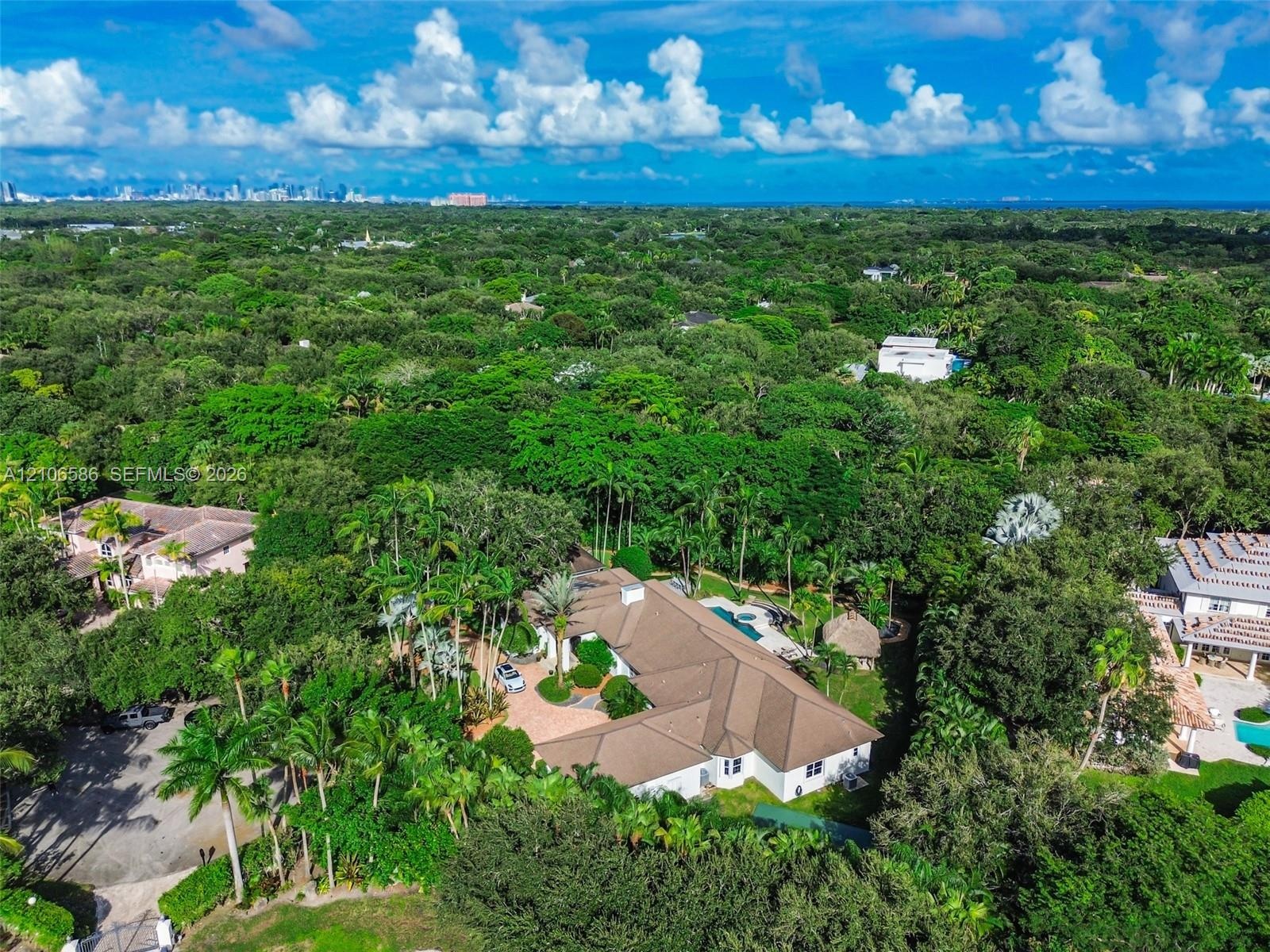 Aerial perspective featuring a multi-gabled roofline, a circular paved driveway, a private swimming pool, and extensive mature landscaping on a heavil