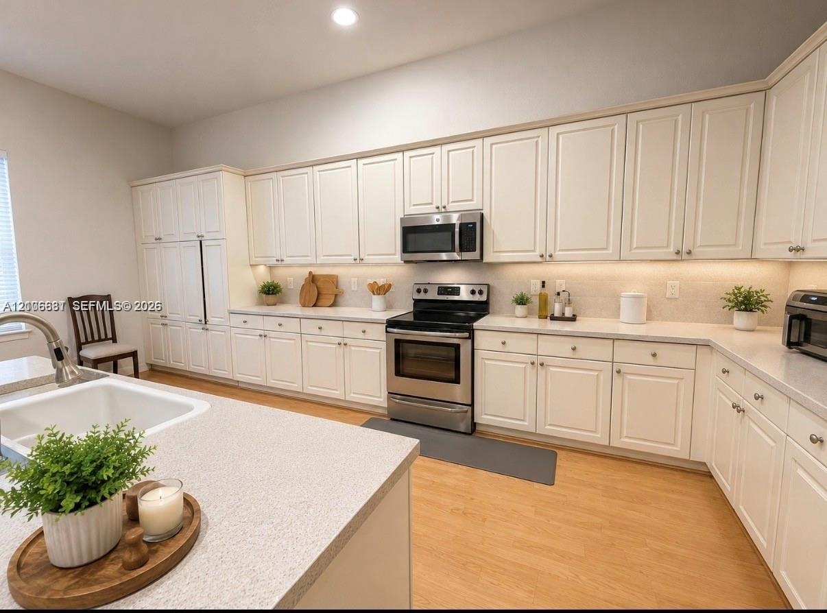 Kitchen featuring white cabinetry, solid-surface countertops, stainless steel appliances, and wood-finish flooring