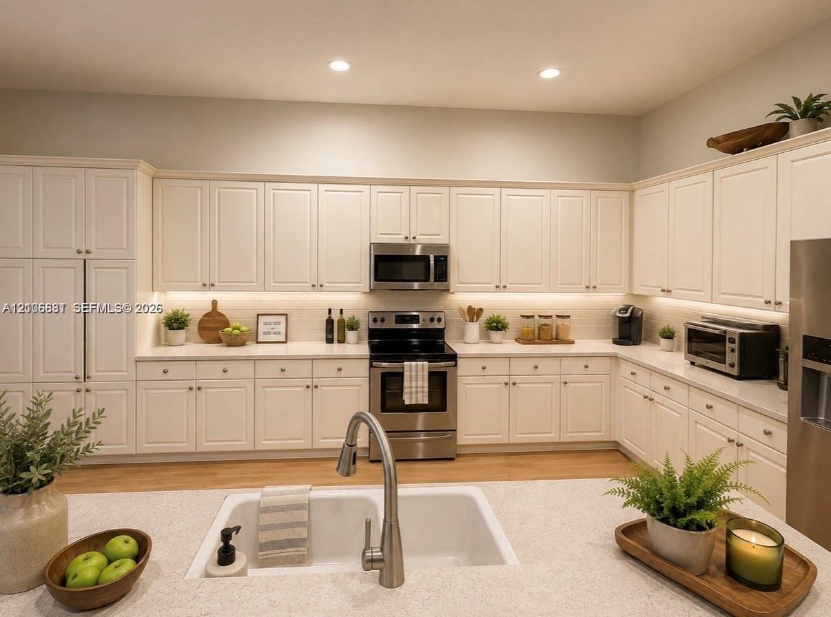 Kitchen featuring white shaker-style cabinetry, stainless steel appliances, under-cabinet lighting, a farmhouse-style sink with a pull-down faucet, an