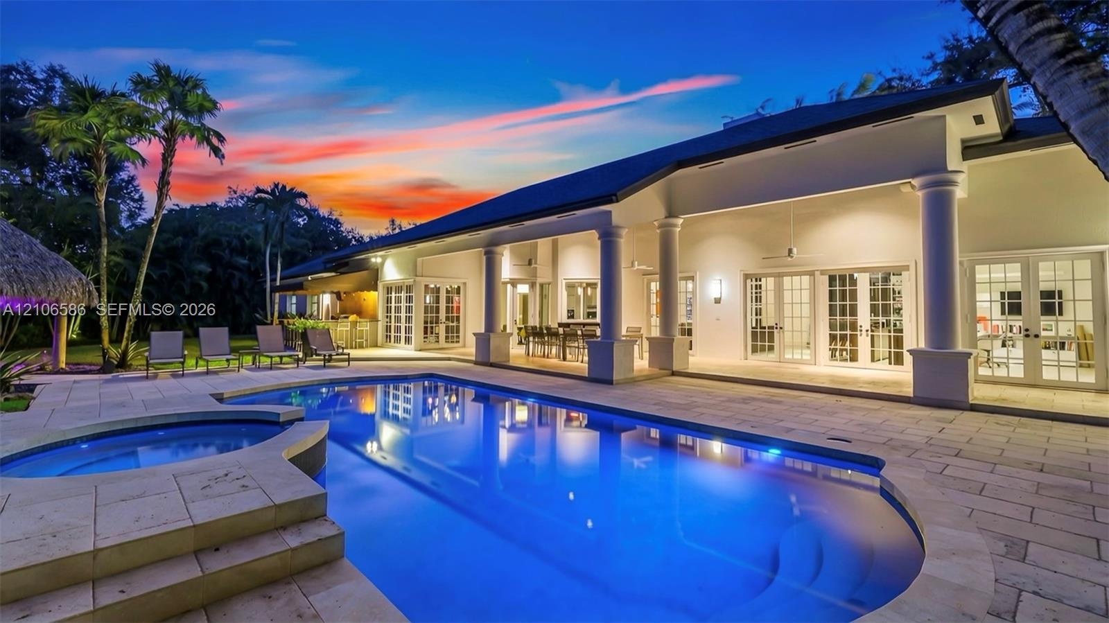 Spacious exterior featuring a covered patio with columns, stone-paved decking, a built-in swimming pool, a separate spa, and multiple sets of French d