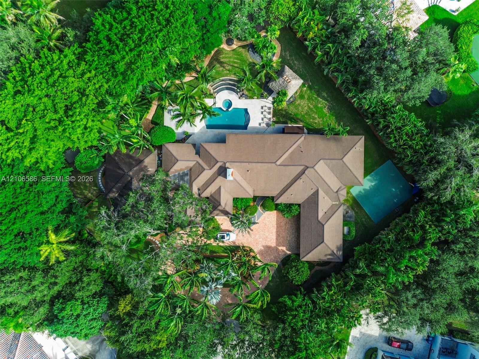 Aerial perspective of a sprawling property featuring a paved circular driveway, a swimming pool with spa, a tennis court, and mature perimeter landsca