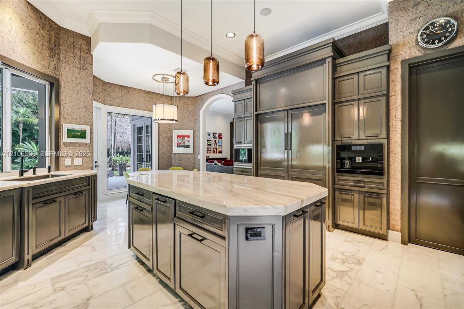 Custom cabinetry with panel-ready integrated appliances, expansive stone-topped central island, polished stone flooring, and multi-pendant lighting