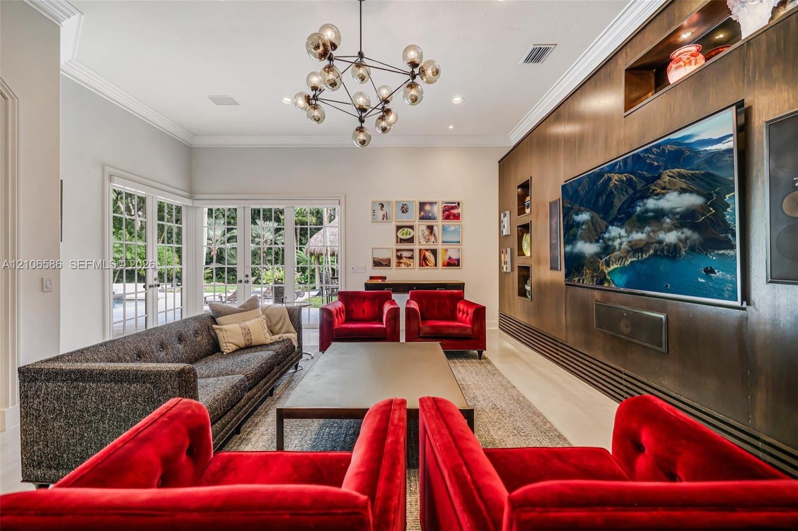 Living area featuring custom wood wall paneling with integrated shelving, multi-globe chandelier, recessed lighting, and full-height glass paneled doo