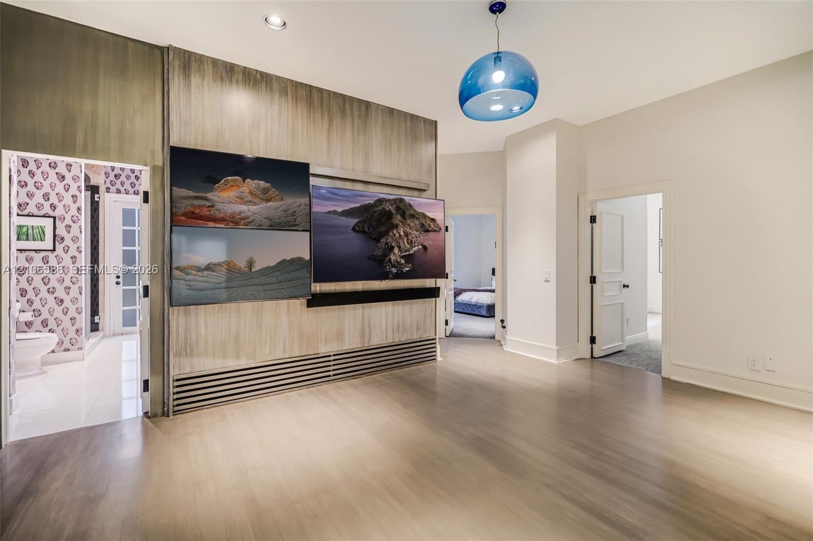 Wood-finish wall paneling with integrated media station, recessed ceiling lighting, and blue glass pendant fixture