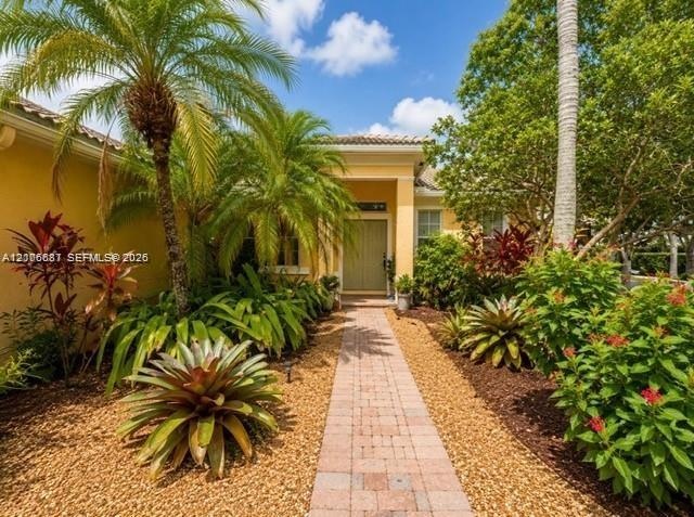 Exterior facade featuring a covered entryway, paved stone walkway, and mature landscaping including palm trees and decorative shrubbery