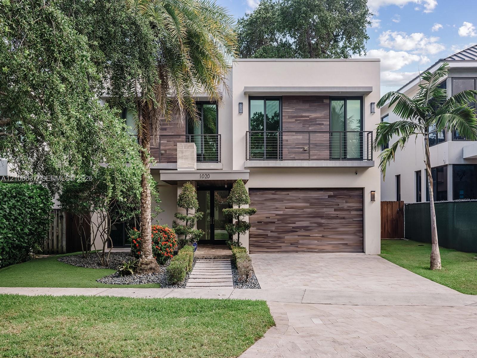 Contemporary two-story exterior featuring wood-finish siding, a private balcony with horizontal metal railings, a modern garage door, and a stone-pave