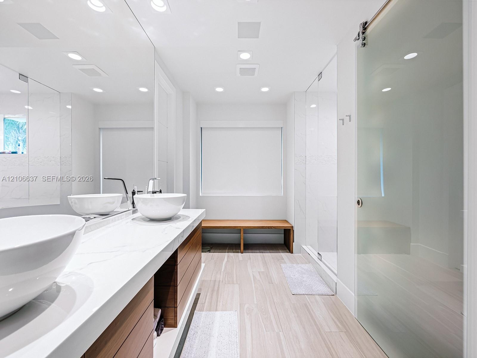 Floating vanity featuring dual vessel sinks, stone-finish countertops, wood-grain cabinetry, and a sliding glass door entry to a walk-in shower