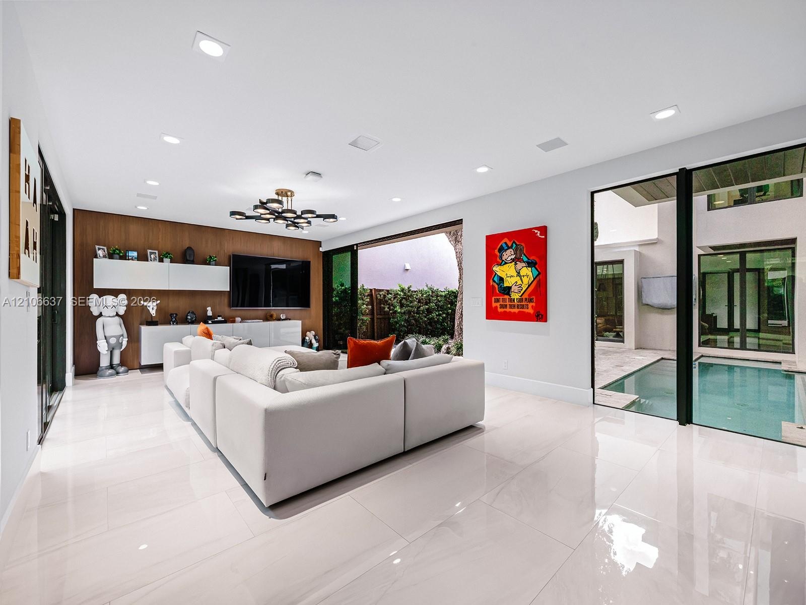 Large-format tile flooring, wood-panel accent wall with integrated built-in cabinetry, recessed ceiling lighting, statement multi-arm chandelier, and 