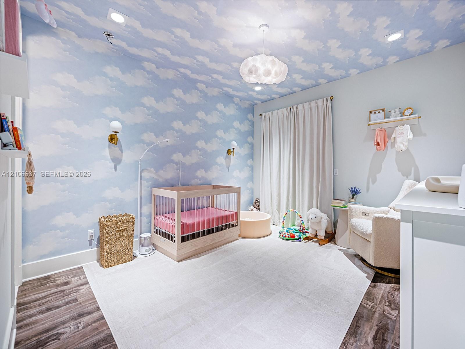 Room featuring cloud-patterned wallpaper extending to the ceiling, wood-finish flooring, dual wall-mounted brass light fixtures, recessed ceiling ligh