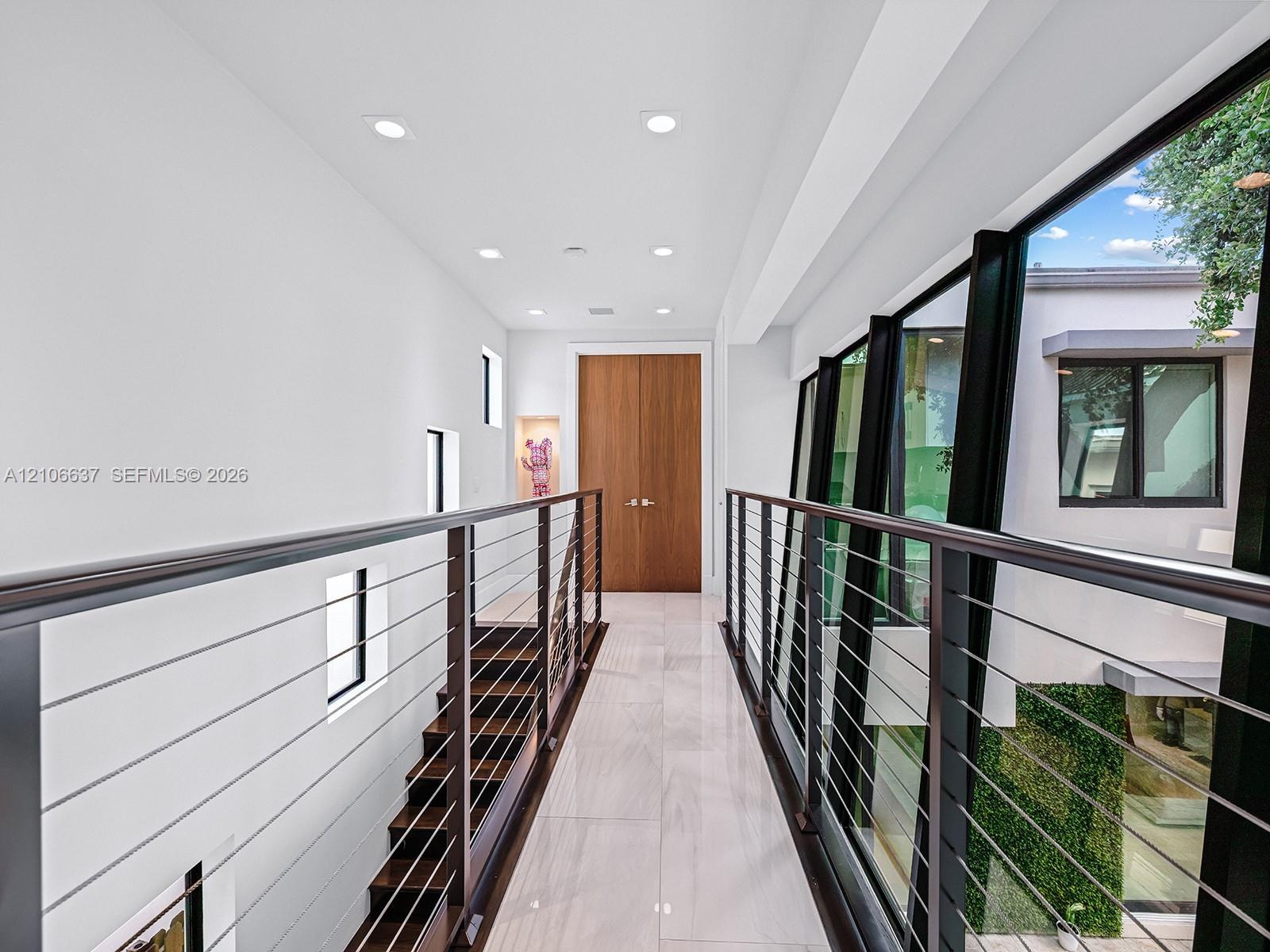 Hallway featuring tile flooring, recessed ceiling lighting, a wood-finish double door, and a cable railing system with a dark metal frame